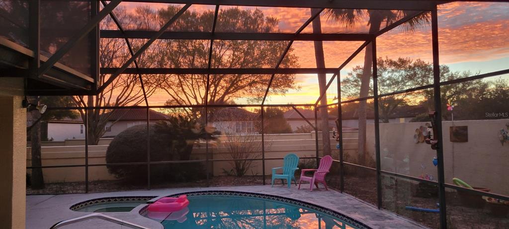 A screened-in pool patio features a small spa, two colorful chairs, and a sunset view — 8215 ROLLA COURT, ORLANDO, FL