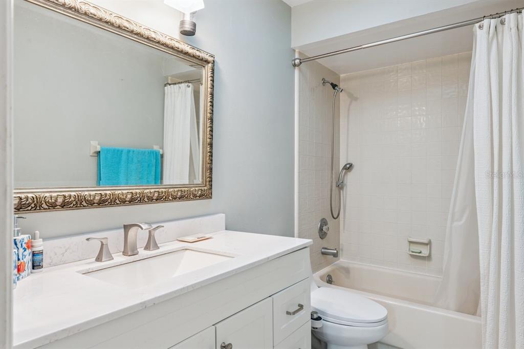 A bathroom features a white vanity with a quartz countertop, a framed mirror, and a tub-shower — 8215 ROLLA COURT, ORLANDO, FL