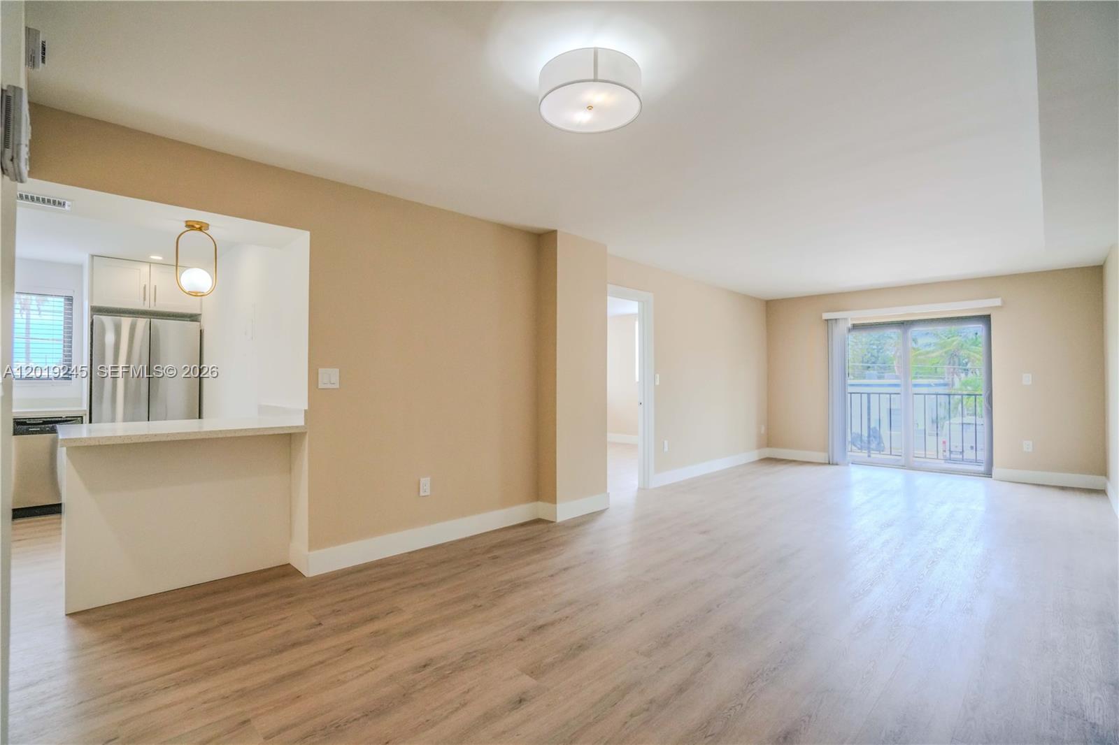 An open-concept living area features light wood-look flooring, a kitchen pass-through, and a balcony door — 6960 Rue Vendome # 201, Miami Beach FL 33141, MIAMI BEACH, FL
