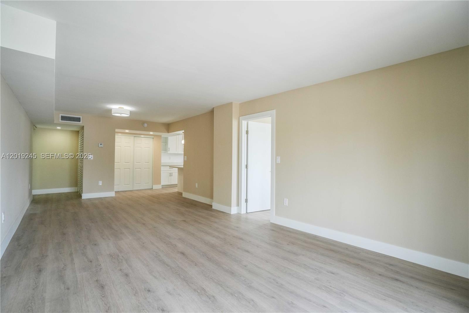 An empty room features light wood-look flooring, beige walls, and a doorway to another area — 6960 Rue Vendome # 201, Miami Beach FL 33141, MIAMI BEACH, FL