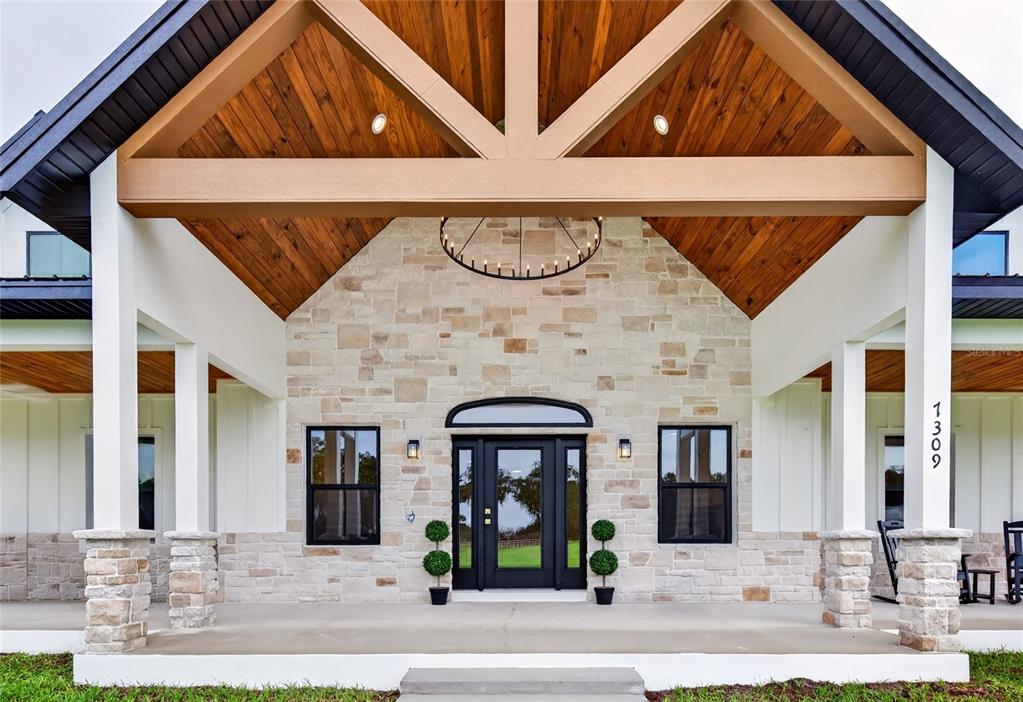 A covered front porch with a stone facade, wood-paneled gable, and black-framed glass front door — 7309 BUSTED OAKS WAY, BUSHNELL, FL
