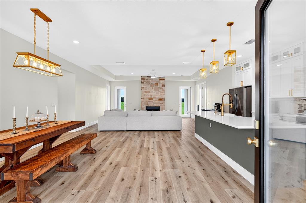 An open-concept living area features a dining table, a stone fireplace, and a kitchen island — 7309 BUSTED OAKS WAY, BUSHNELL, FL