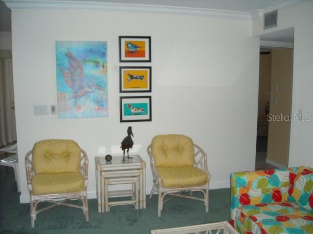 A living room features two yellow wicker chairs, a nesting table, and colorful wall art — 1700 GLENHOUSE DRIVE UNIT 305, SARASOTA, FL