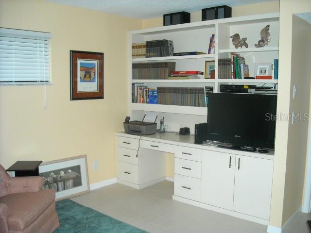 A home office features a built-in desk, shelving unit, television, and light-colored tile flooring — 1700 GLENHOUSE DRIVE UNIT 305, SARASOTA, FL