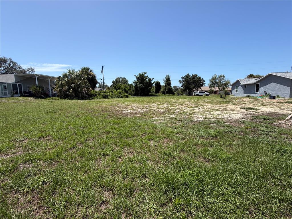 A grassy, vacant residential lot sits between two existing houses under a clear blue sky — 5540 BAFFIN CIRCLE, SPRING HILL, FL