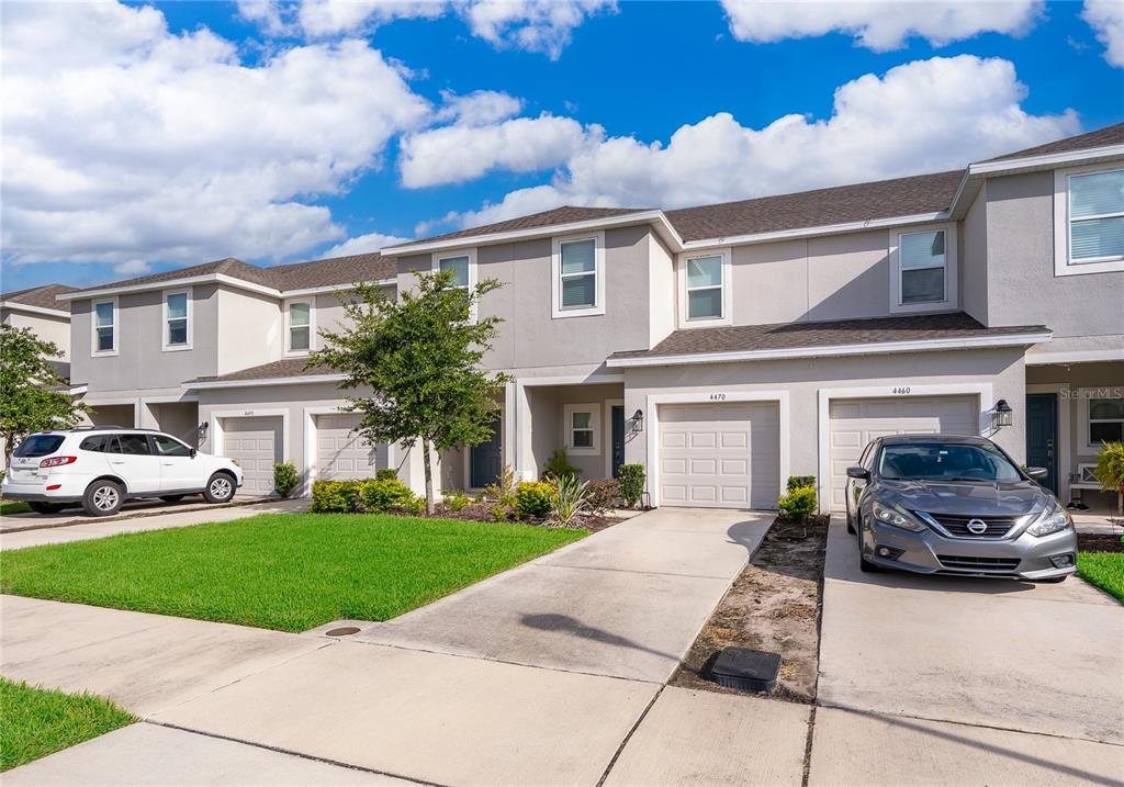 A row of two-story townhouses with beige stucco exteriors, attached garages, and concrete driveways — 4470 CALVARY WAY, ST CLOUD, FL