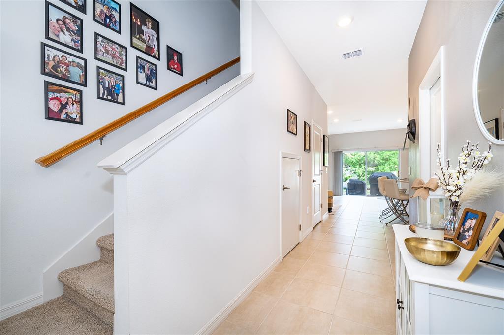 A hallway features a carpeted staircase with a gallery wall and tiled flooring leading outside — 4470 CALVARY WAY, ST CLOUD, FL