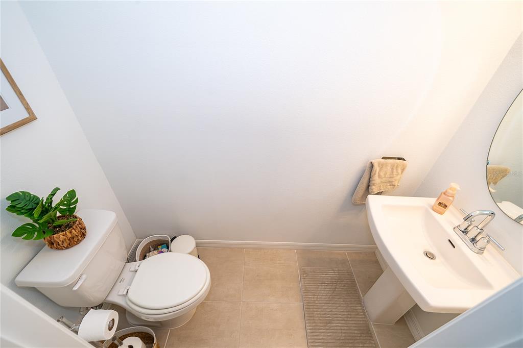 A small powder room features a pedestal sink, a white toilet, and beige floor tiles — 4470 CALVARY WAY, ST CLOUD, FL