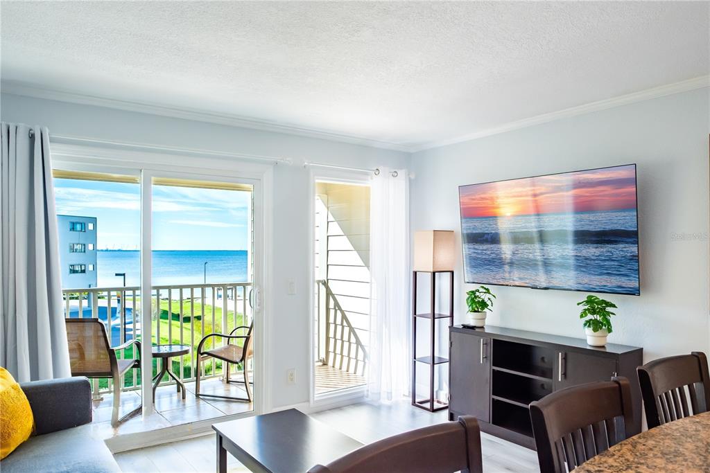 A living room with a wall-mounted television, dark furniture, and a balcony overlooking the ocean — 2506 N ROCKY POINT DRIVE UNIT 301, TAMPA, FL