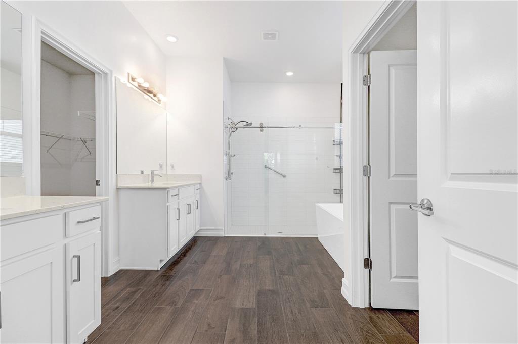 A modern bathroom features a double vanity, a glass-enclosed shower, and dark wood-look flooring — 12876 BERGSTROM BAY DRIVE, RIVERVIEW, FL