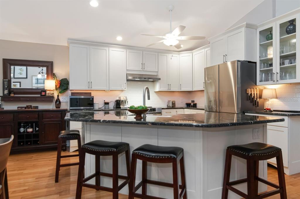 A kitchen with white cabinets, a dark granite island, and three dark wooden bar stools — 940 WISCONSIN AVENUE, PALM HARBOR, FL