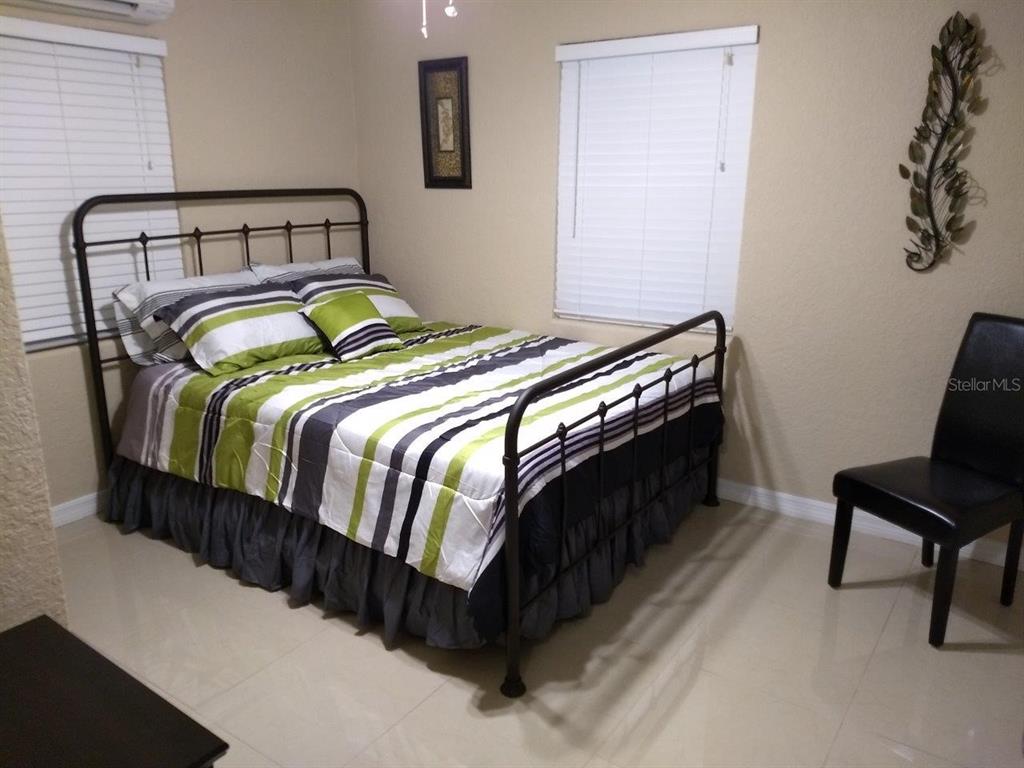 A bedroom features a metal-framed bed with striped bedding, tile flooring, and two windows — 2512 MUSSELWHITE AVENUE UNIT #1, ORLANDO, FL