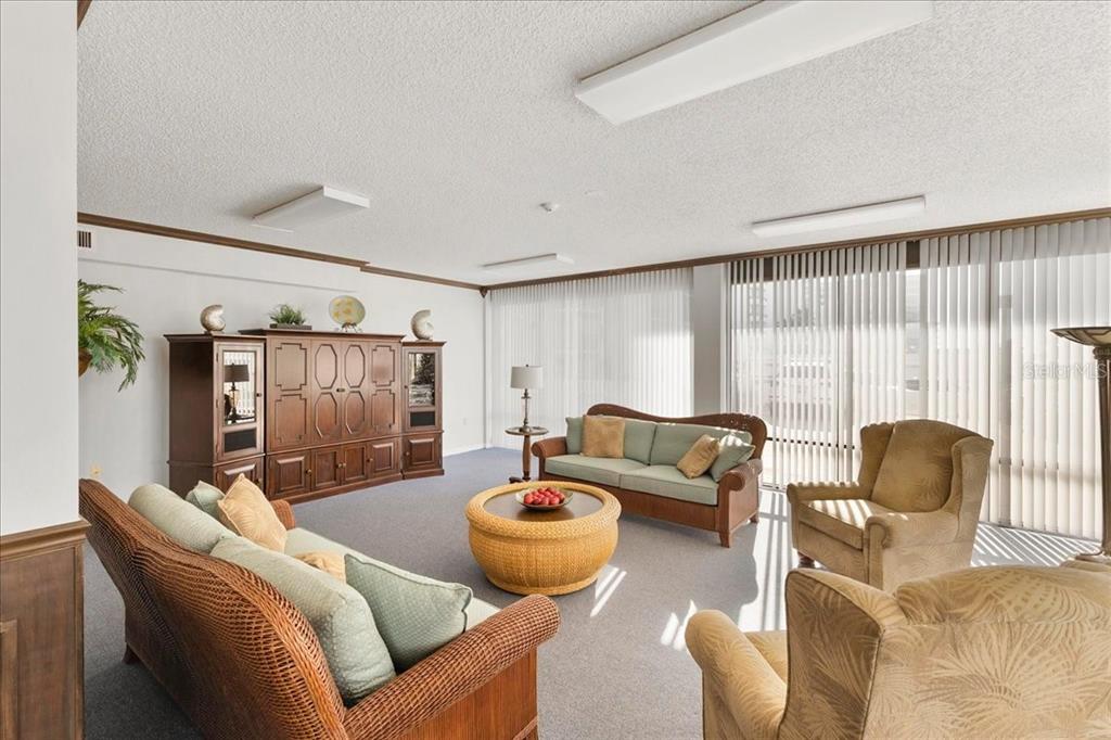 A living room features wicker furniture, a large wooden entertainment center, and vertical window blinds — 3743 S ATLANTIC AVENUE UNIT 10B0, DAYTONA BEACH, FL