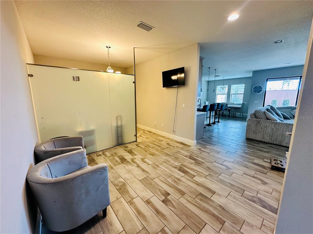 A living area features wood-look tile flooring, two grey armchairs, and a frosted glass partition — 12990 BURNS DRIVE, ODESSA, FL