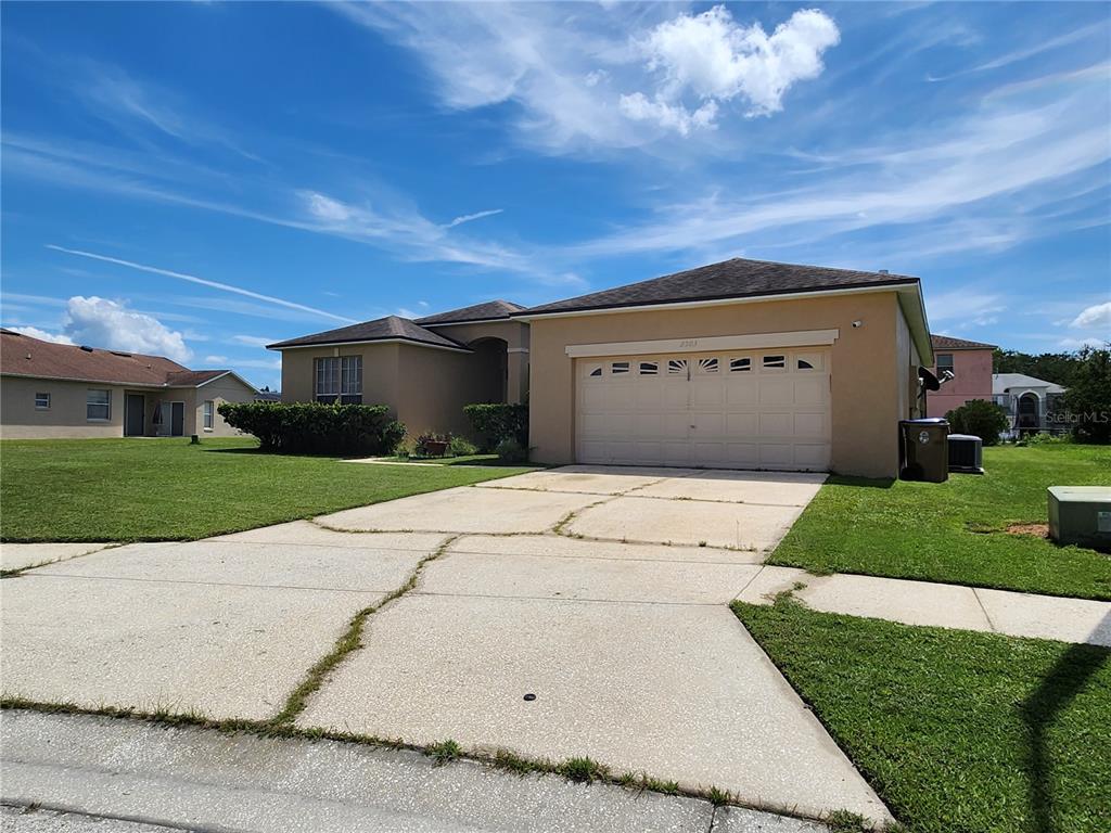 A tan single-story house with a two-car garage and a cracked concrete driveway — 2503 BUTTERCUP COURT, KISSIMMEE, FL