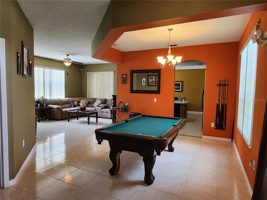 A pool table sits in a tiled room with orange walls next to a living area — 2503 BUTTERCUP COURT, KISSIMMEE, FL