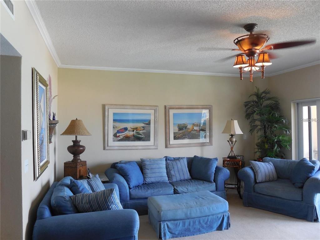 A living room features blue sofas, an ottoman, two framed beach paintings, and a ceiling fan — 880 MANDALAY AVENUE UNIT S705, CLEARWATER, FL