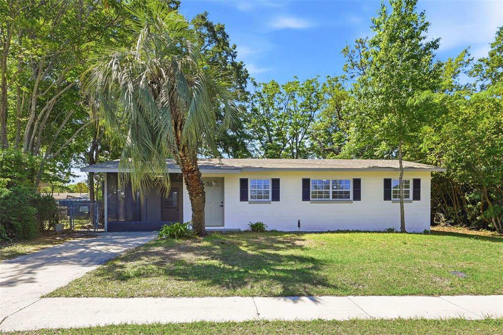 A single-story white house with a screened porch, a palm tree, and a concrete driveway — 2115 WOODLAND BOULEVARD, LEESBURG, FL