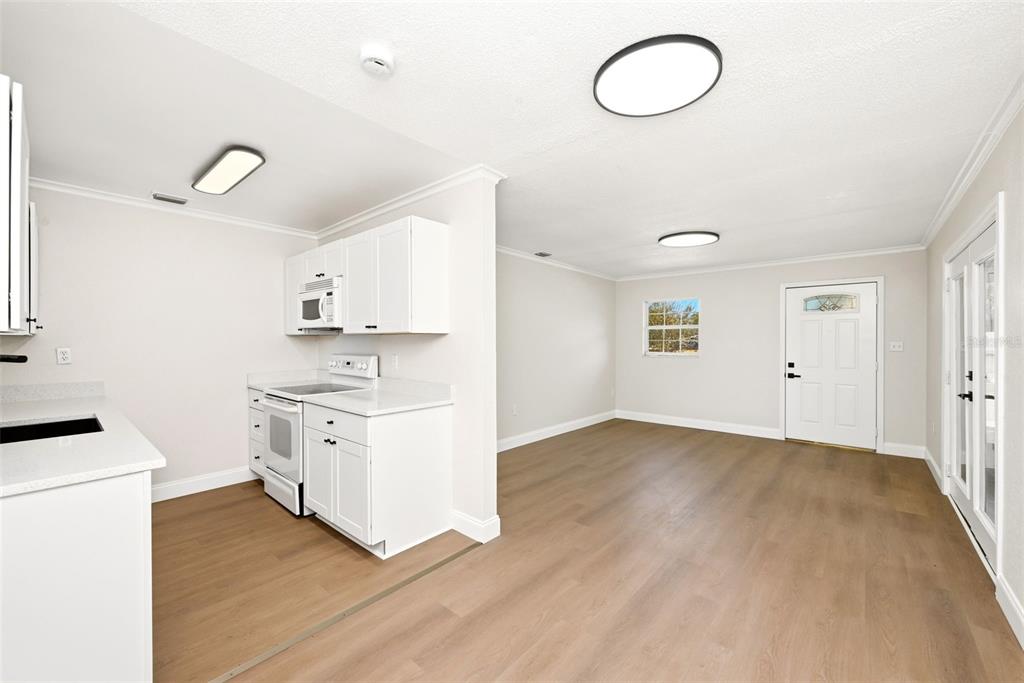 A kitchen with white cabinets and appliances opens into a living area with wood flooring — 2115 WOODLAND BOULEVARD, LEESBURG, FL