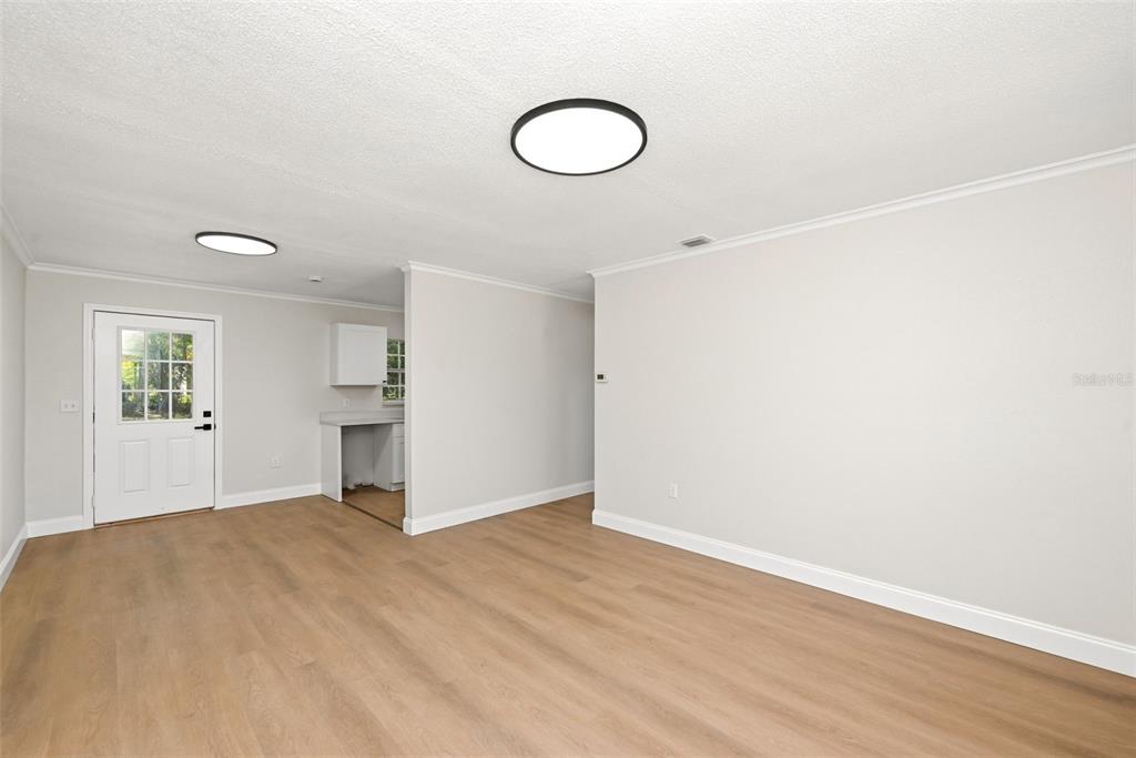 A bright, empty room features light wood-look flooring, white walls, and two modern ceiling lights — 2115 WOODLAND BOULEVARD, LEESBURG, FL