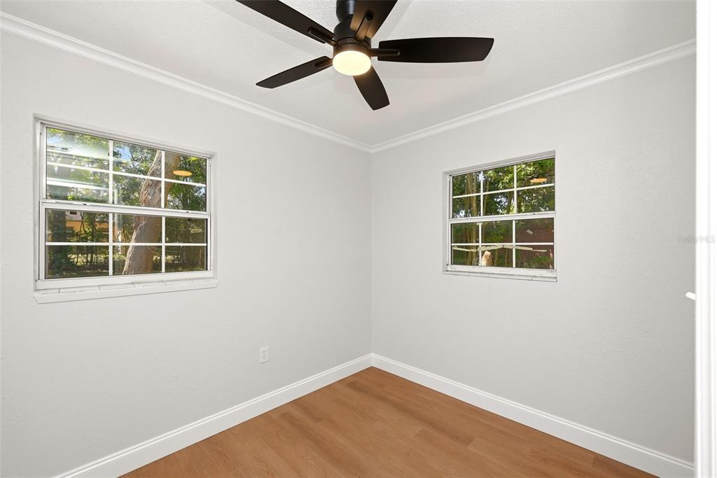An empty bedroom features white walls, light wood-look flooring, a ceiling fan, and two windows — 2115 WOODLAND BOULEVARD, LEESBURG, FL