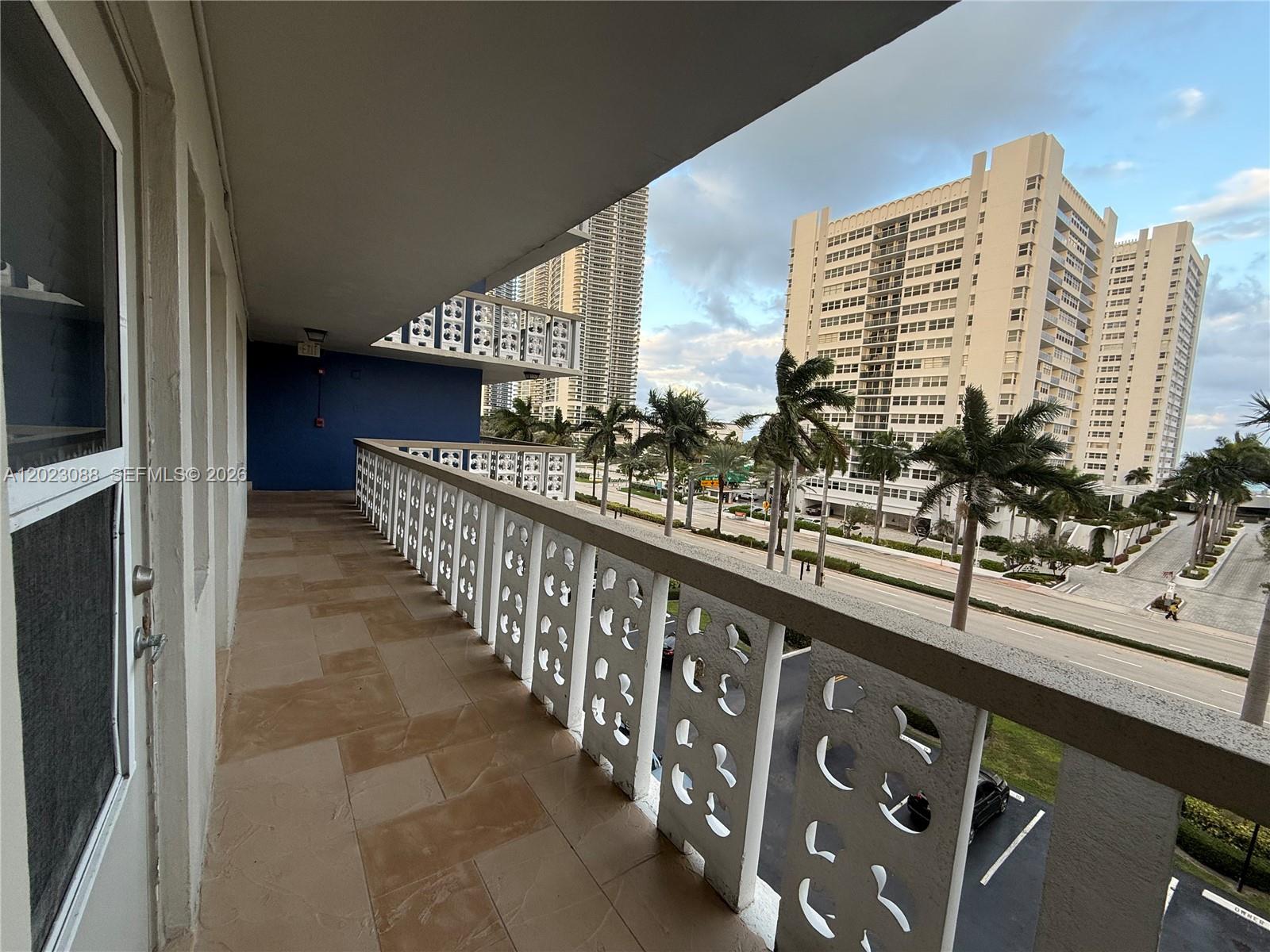 A balcony with patterned white railings overlooks a street, palm trees, and neighboring high-rise buildings — 1893 S Ocean Dr # 506, Hallandale Beach FL 33009, HALLANDALE BEACH, FL