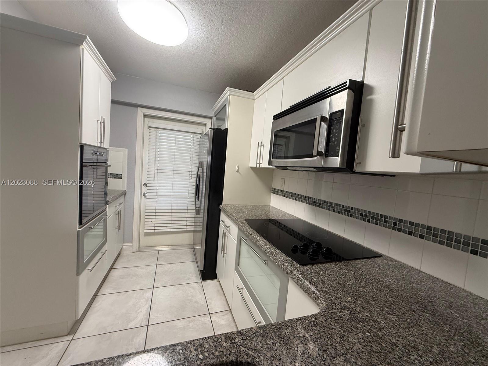 A galley kitchen features white cabinets, granite countertops, stainless steel appliances, and tile flooring — 1893 S Ocean Dr # 506, Hallandale Beach FL 33009, HALLANDALE BEACH, FL