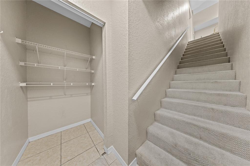A tiled storage closet with wire shelving sits beside a carpeted staircase with a handrail — 6340 RALEIGH STREET UNIT 1011, ORLANDO, FL