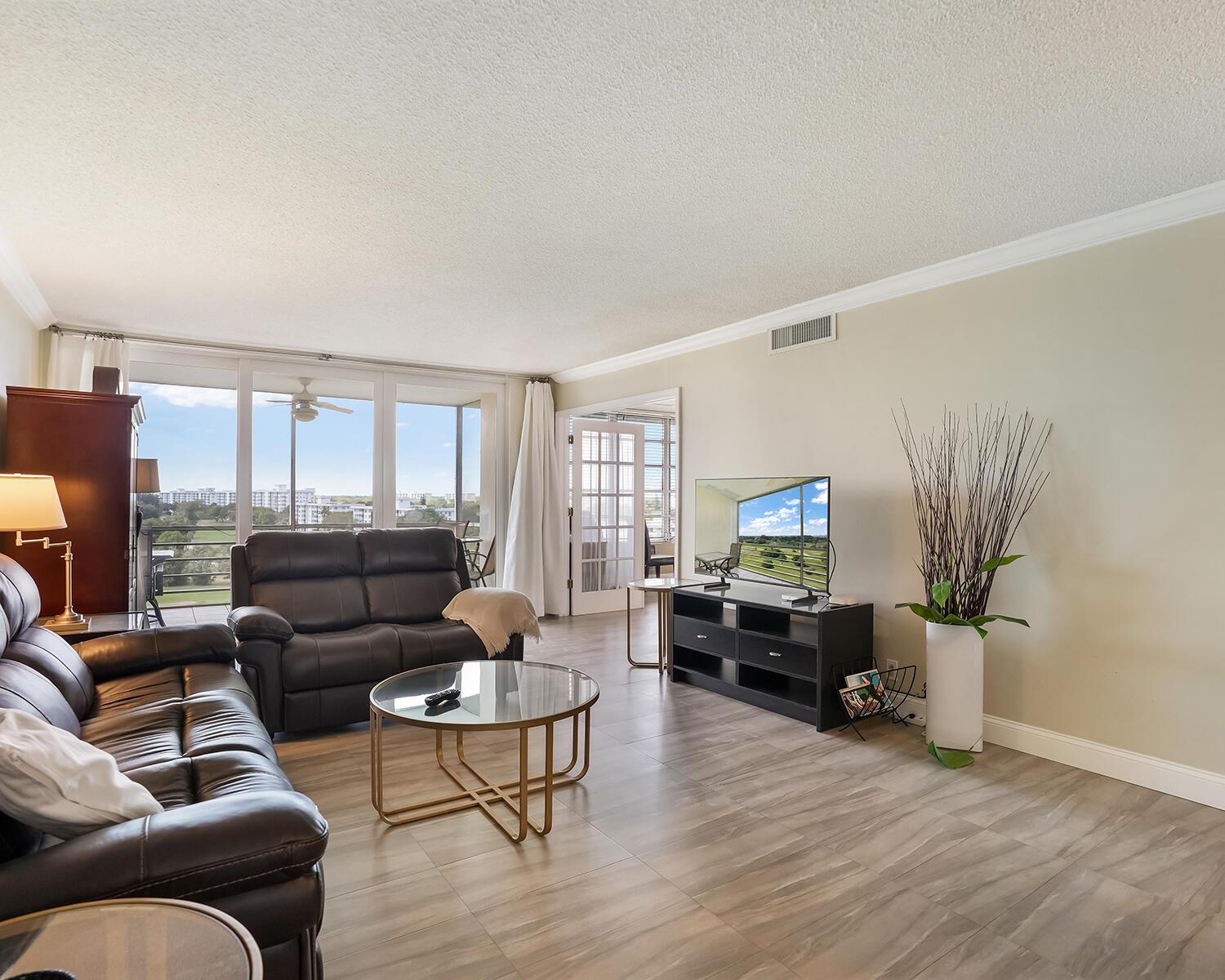 A living room features dark leather sofas, a glass coffee table, and a television console — 2671 S Course Drive # 907, Pompano Beach FL 33069, POMPANO BEACH, FL