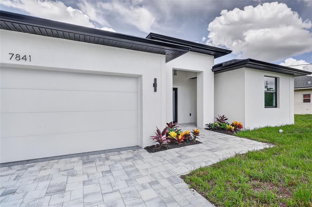 The exterior of a modern white house features a garage, a paved walkway, and landscaping — 7841 SONTAG AVENUE, NORTH PORT, FL