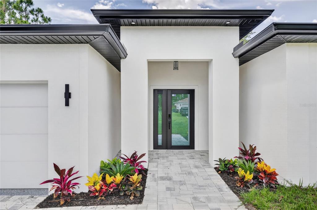 The front exterior of a modern white house features a glass-paneled door and landscaping — 7841 SONTAG AVENUE, NORTH PORT, FL