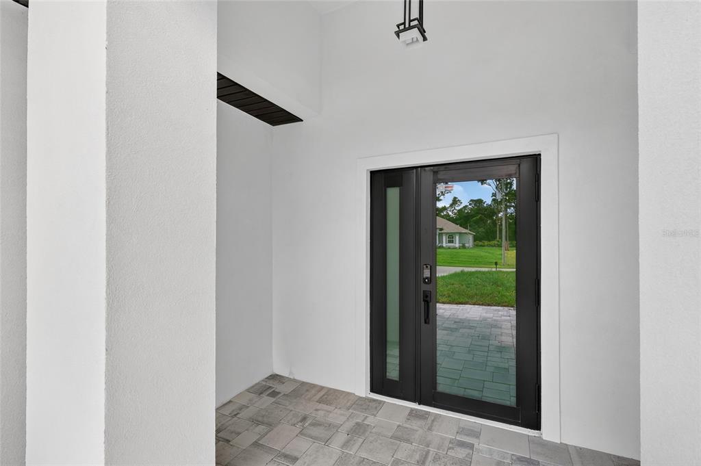 A modern front entrance features a black glass door, white walls, and stone paver flooring — 7841 SONTAG AVENUE, NORTH PORT, FL