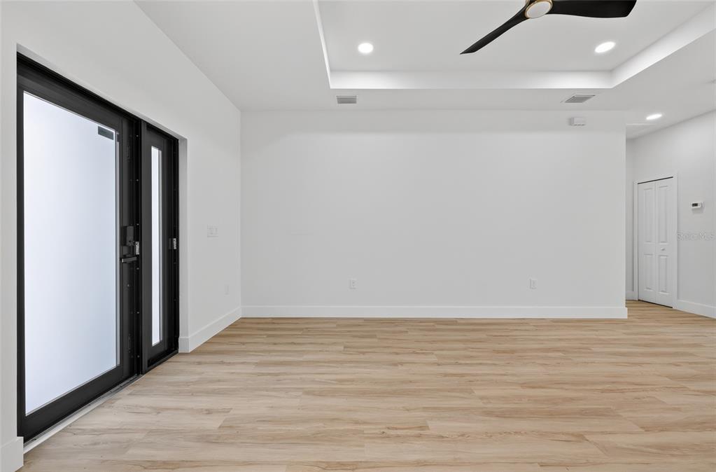 A bright, empty room features light wood-look flooring, white walls, and black-framed glass doors — 7841 SONTAG AVENUE, NORTH PORT, FL