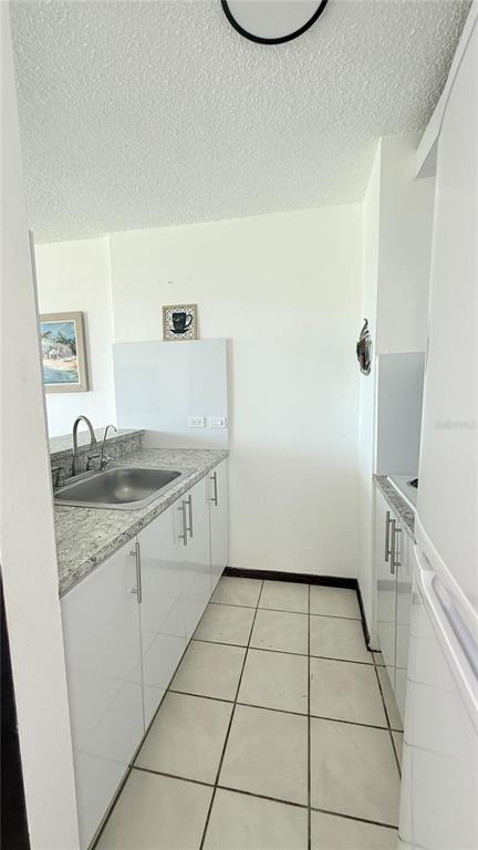 A galley kitchen features white cabinets, granite countertops, a stainless steel sink, and tiled flooring — AVENIDA MARINA VIEW DOS MARINAS II UNIT 908, FAJARDO, PR