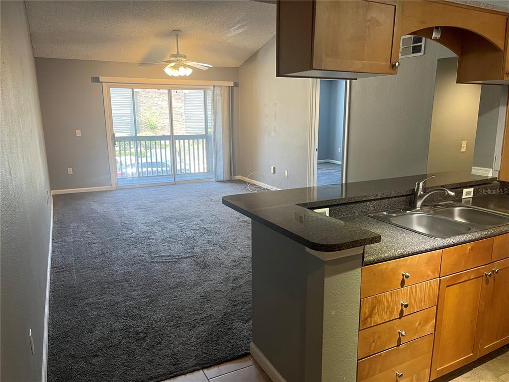A view from a kitchen with wooden cabinets toward a carpeted living area with sliding doors — 2500 WINDING CREEK BOULEVARD UNIT C205, CLEARWATER, FL