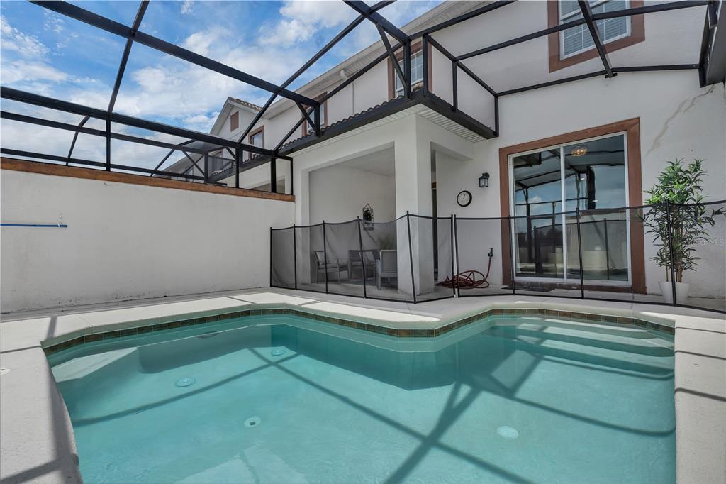 A swimming pool with a safety fence sits under a screened lanai behind a house — 9005 STINGER DRIVE, DAVENPORT, FL
