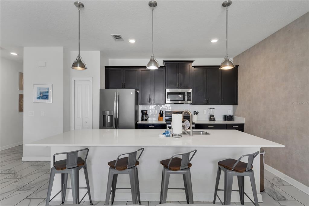 A modern kitchen features dark cabinets, a white quartz island, and four metal bar stools — 9005 STINGER DRIVE, DAVENPORT, FL
