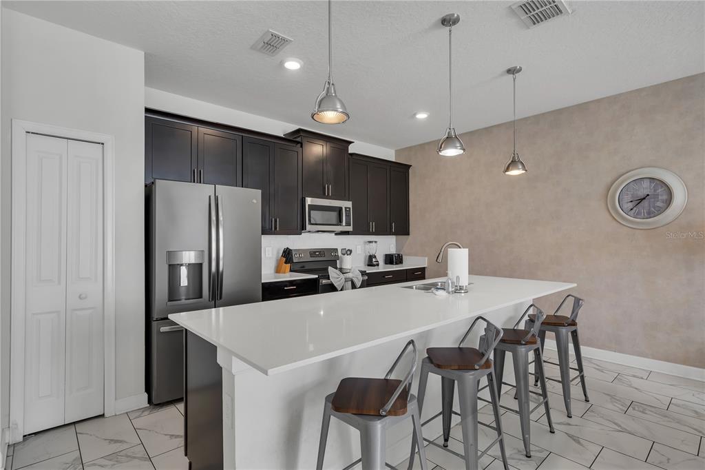 A kitchen features dark cabinets, stainless steel appliances, a white island, and three metal stools — 9005 STINGER DRIVE, DAVENPORT, FL