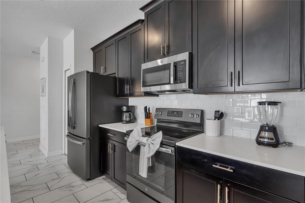 A kitchen features dark wood cabinets, stainless steel appliances, white countertops, and white subway tile — 9005 STINGER DRIVE, DAVENPORT, FL