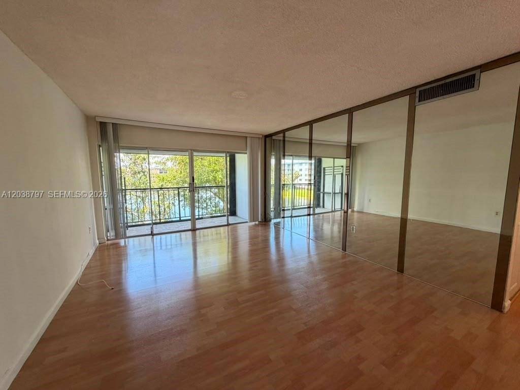 An empty room features wood-look flooring, a sliding glass door, and mirrored closet doors — 8775 Park Blvd # 318, Miami FL 33172, MIAMI, FL