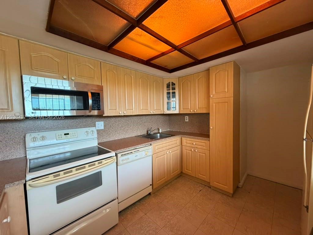 A kitchen features light wood cabinets, white appliances, a tiled floor, and a grid ceiling — 8775 Park Blvd # 318, Miami FL 33172, MIAMI, FL