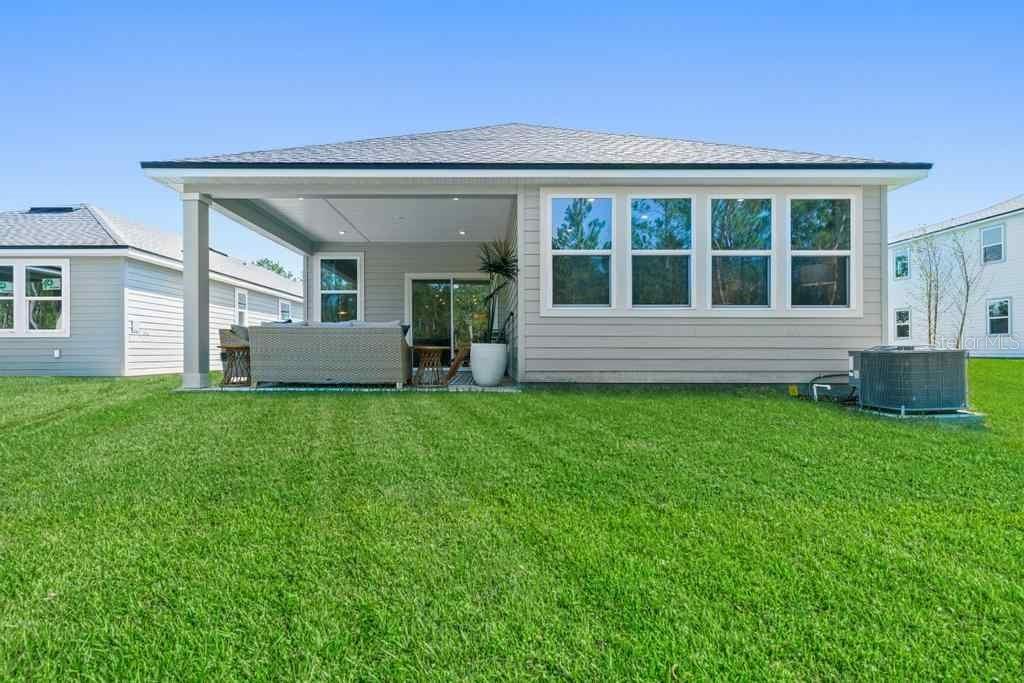 The back exterior of a single-story house features a covered patio and a grassy yard — 1357 RIBBON PLACE, PALM COAST, FL