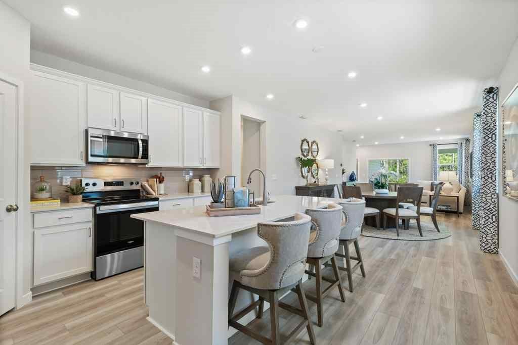 A modern kitchen with white cabinets, a central island, and bar seating opens to dining — 1357 RIBBON PLACE, PALM COAST, FL