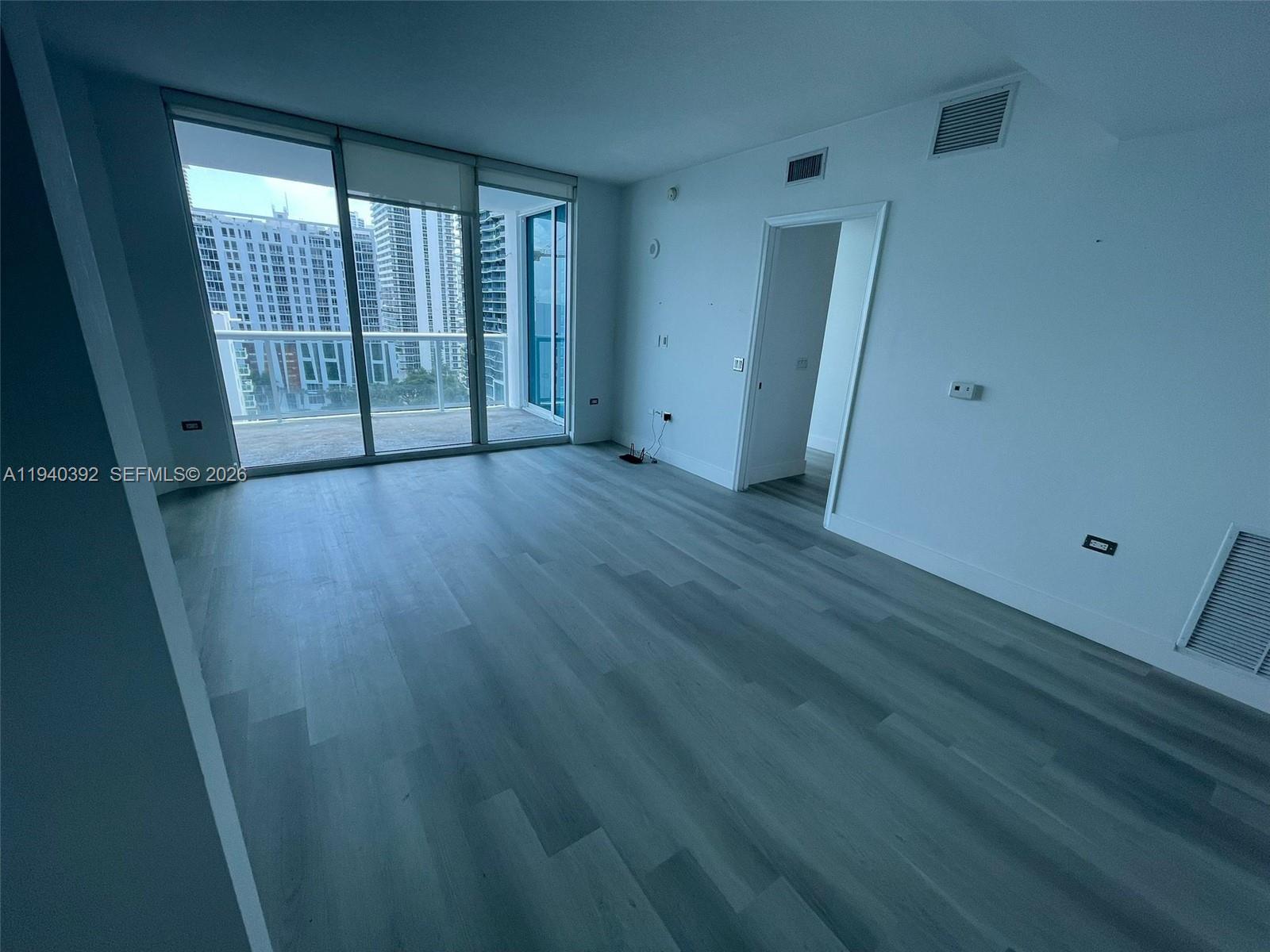 An empty room features light wood-look flooring, white walls, and a balcony with city views — 480 NE 30th St # 1403, Miami FL 33137, MIAMI, FL