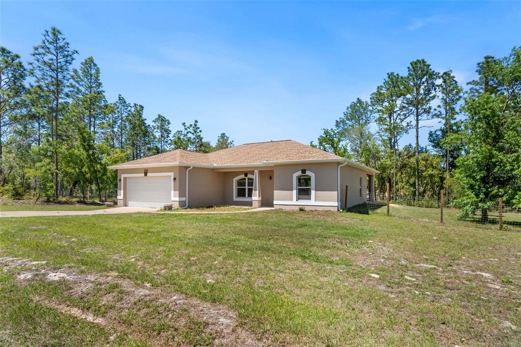 A single-story tan house with a two-car garage sits on a grassy, wooded lot — 13391 RUFFED GROUSE ROAD, WEEKI WACHEE, FL