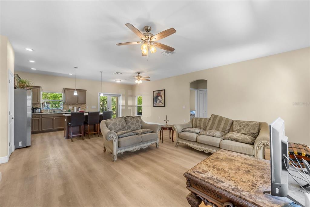 An open-concept living room and kitchen featuring light wood flooring, neutral walls, and ceiling fans — 13391 RUFFED GROUSE ROAD, WEEKI WACHEE, FL