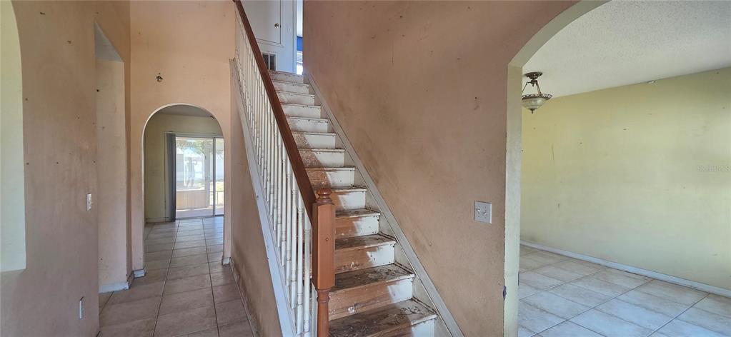 An interior view shows a staircase with wooden treads and white railings between two rooms — 810 DENGAR AVENUE, HAINES CITY, FL