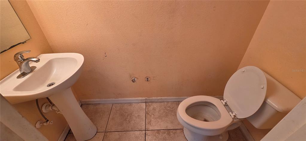 A small bathroom features a pedestal sink, a white toilet, and light-colored floor tiles — 810 DENGAR AVENUE, HAINES CITY, FL