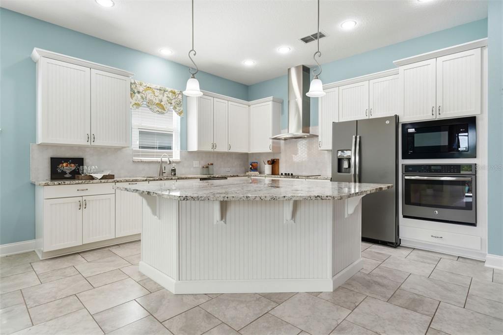 A kitchen with white beadboard cabinetry, a large granite island, and stainless steel appliances — 16716 ABBEY HILL COURT, CLERMONT, FL