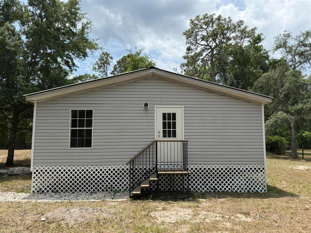 The exterior of a light gray manufactured home features a white door, stairs, and lattice skirting — 10405 JUNGLE STREET, NEW PORT RICHEY, FL